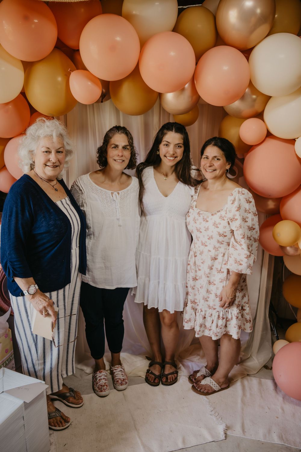 Four women smiling together in front of a peach balloon arch at a bridal shower celebration.