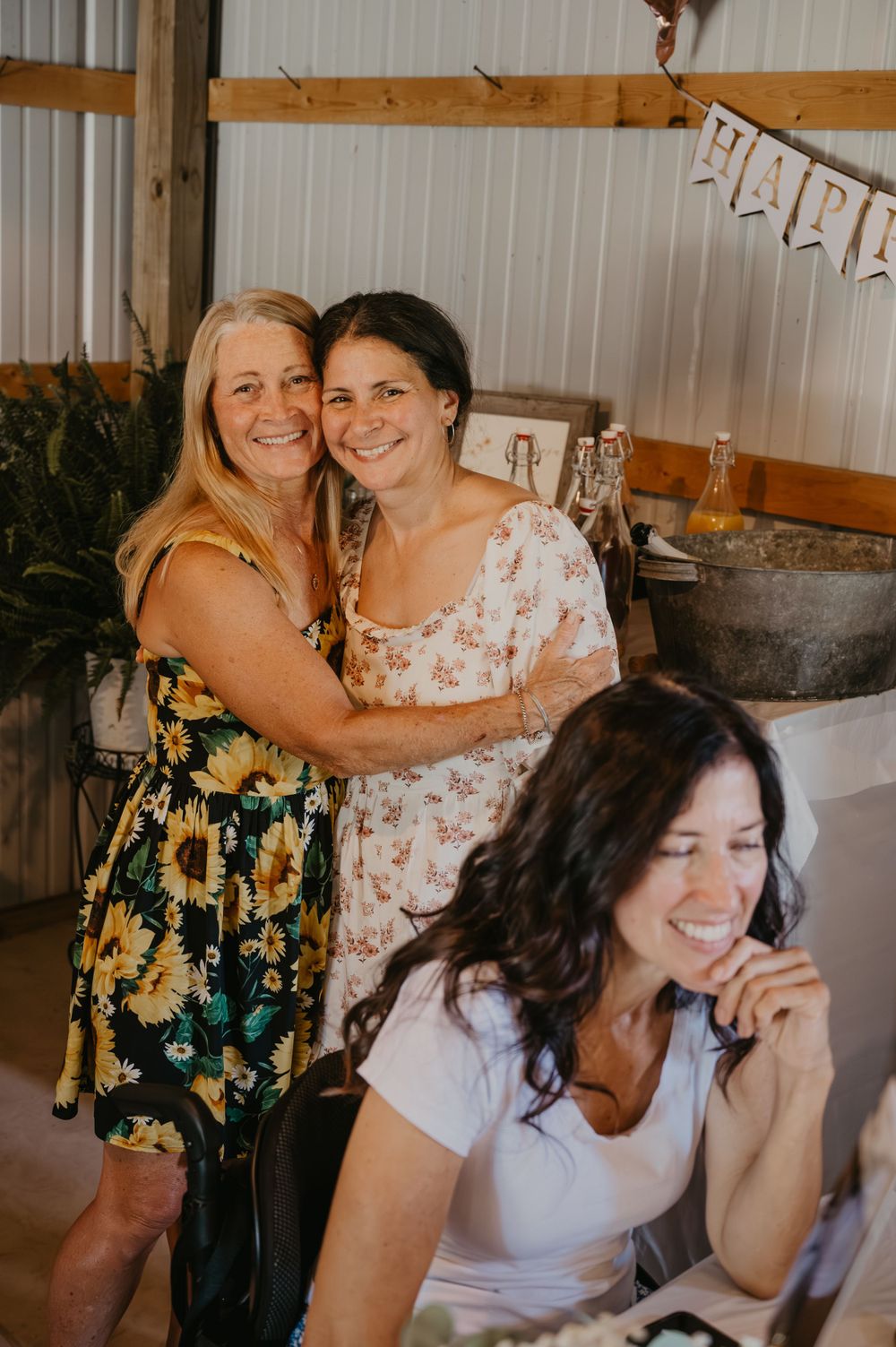 Two women smiling and hugging at a rustic barn bridal shower celebration.