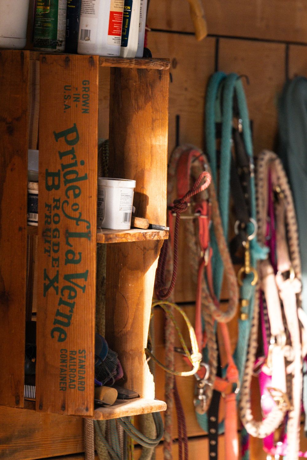 Wooden spools with colorful ribbons and trims arranged on rustic shelving in warm lighting.
