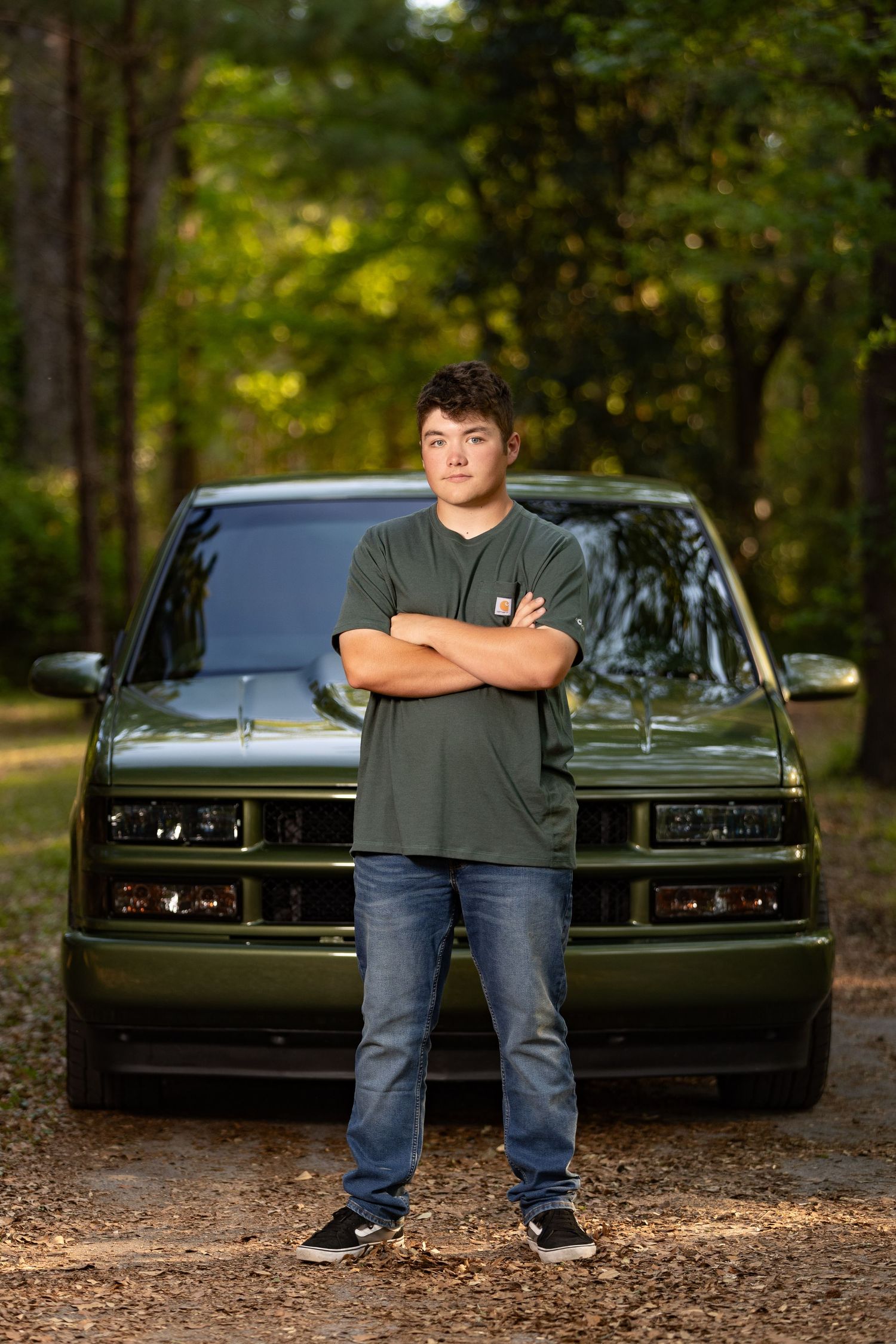 Classic dark green muscle car parked in wooded area during photoshoot.