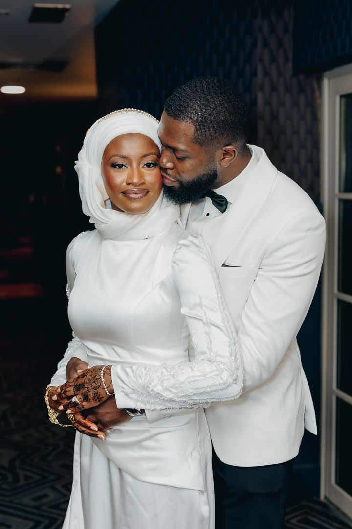 Elegant wedding couple in white attire embracing during intimate moment.