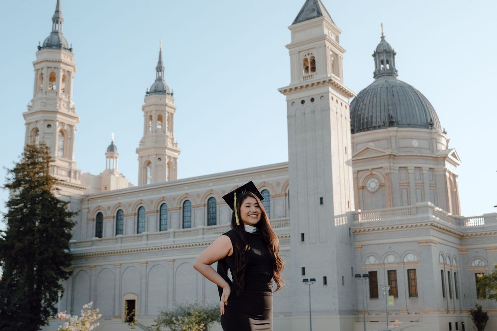 A graduate poses in front of the ornate white domed facade of St. Paul Seminary in Minnesota during commencement.