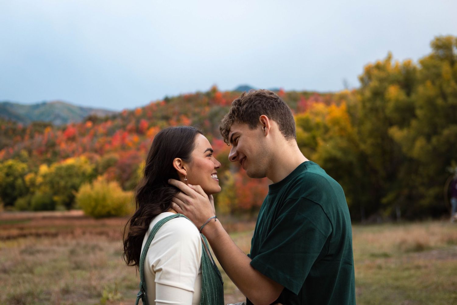 A couple facing each other smiling with fall colors behind them