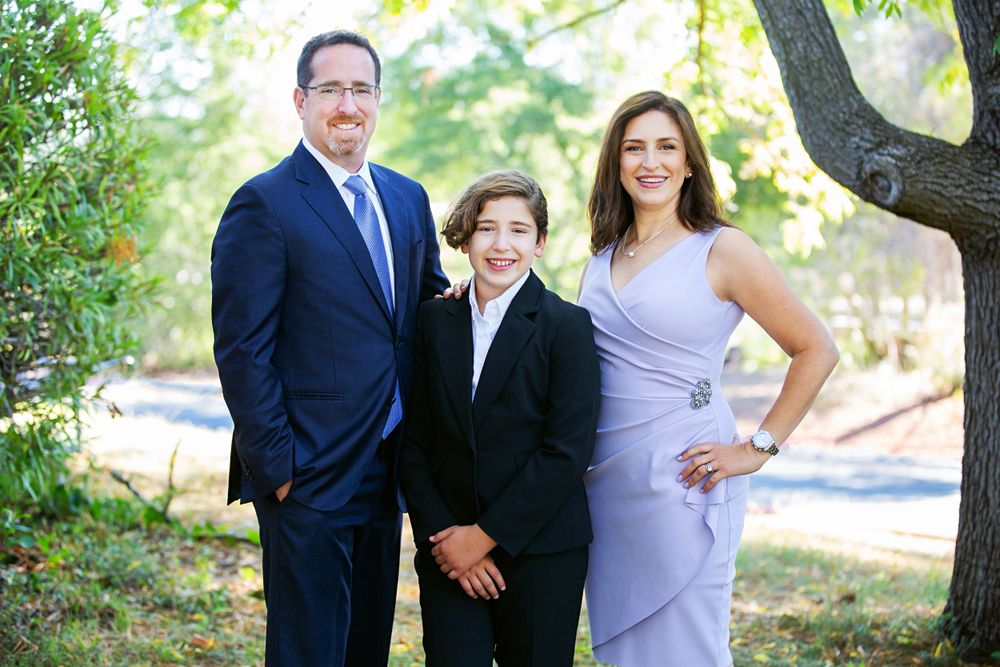 A family dressed in formal attire poses outdoors together against a natural background with trees and greenery.