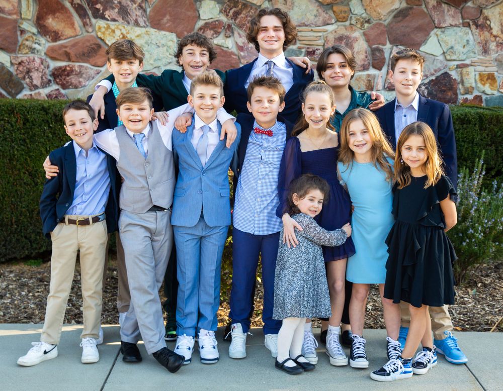 Group of young children dressed in formal attire including blue suits, navy dresses, and matching outfits standing together outdoors.