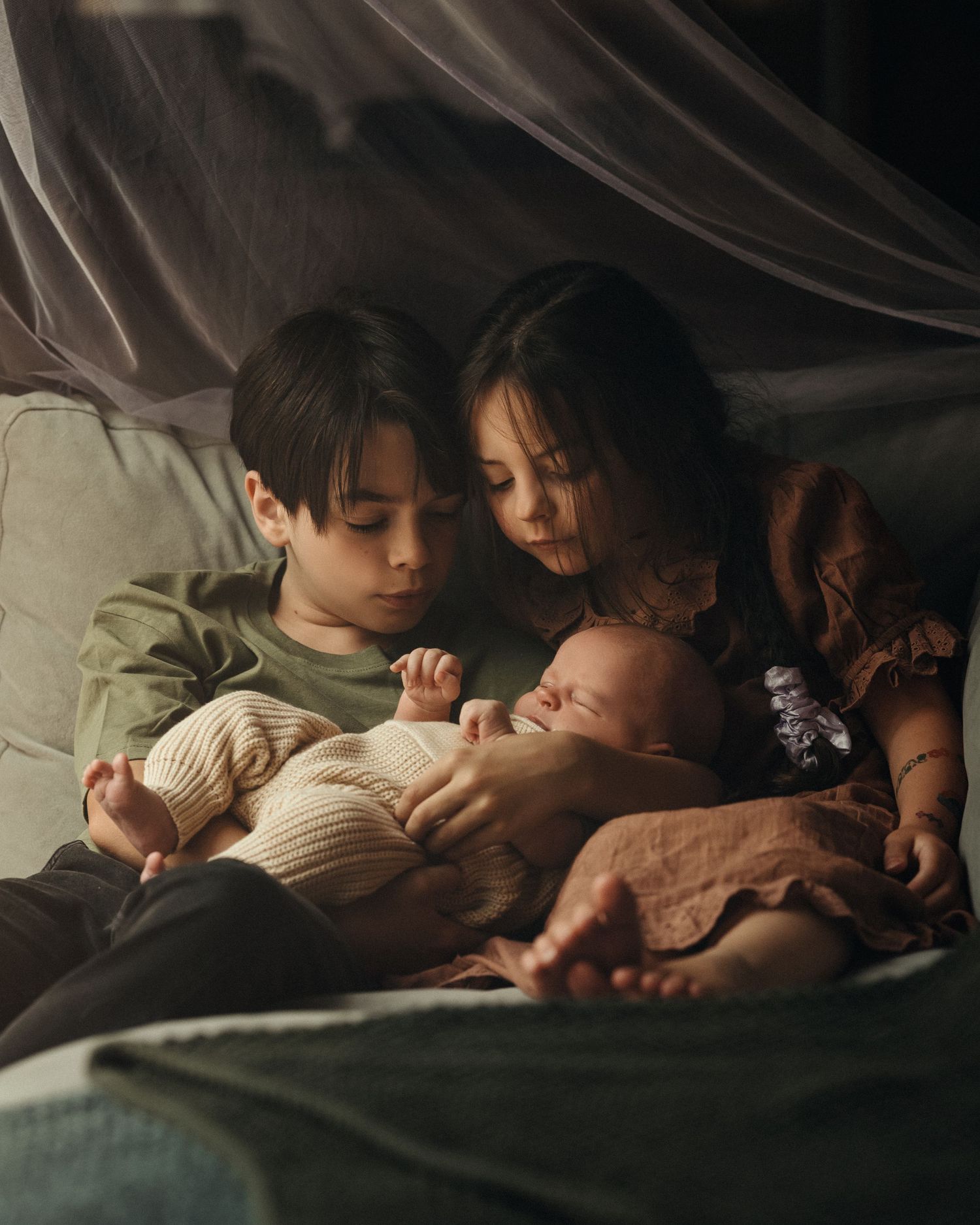 Siblings cuddled up with baby – tender in-home lifestyle session with newborn
