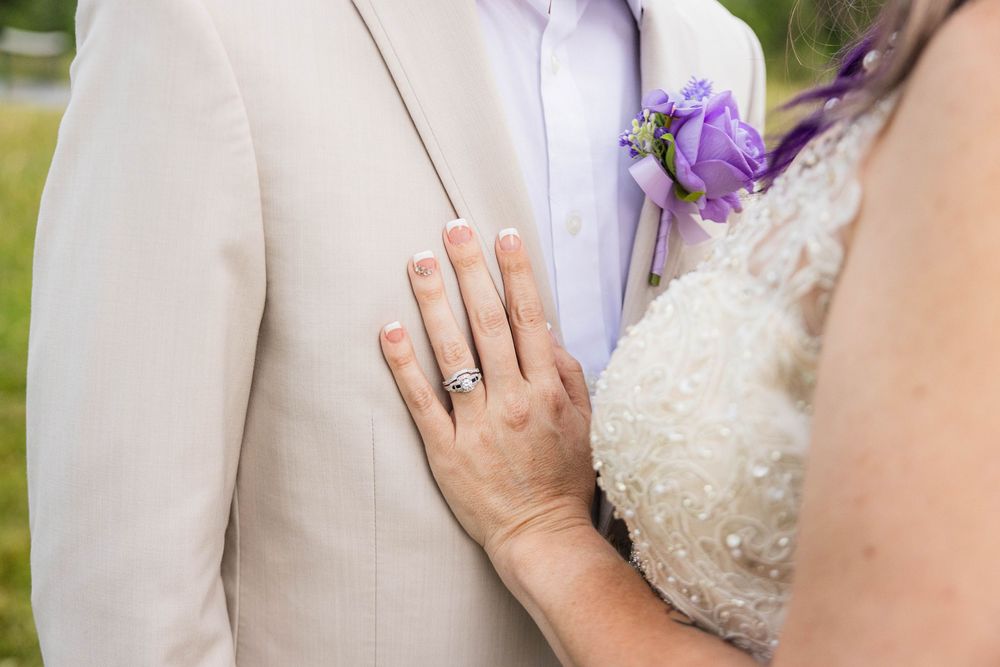 Couple in wedding attire holding hands and embracing during outdoor photo session with purple flowers.