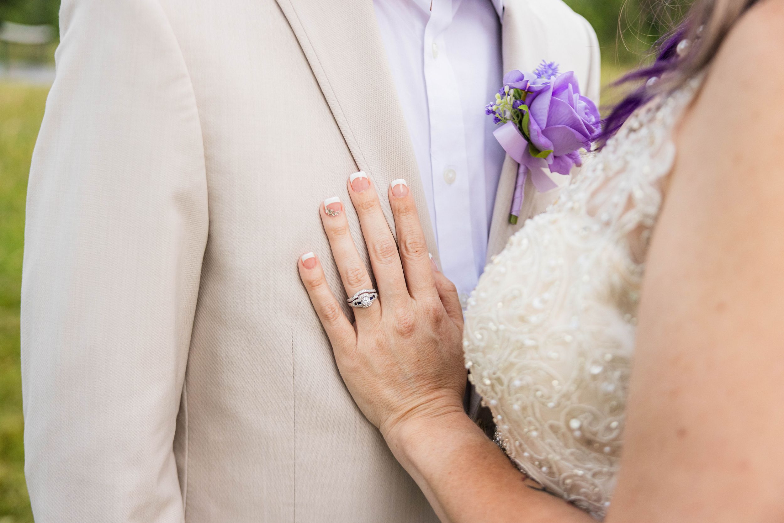 Couple in wedding attire holding hands and embracing during outdoor photo session with purple flowers.