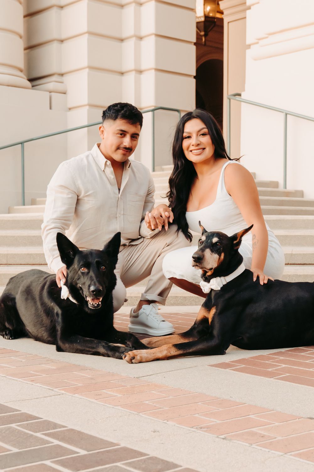 A couple relaxes on tile flooring with their black dog enjoying a casual moment together at a building entrance.
