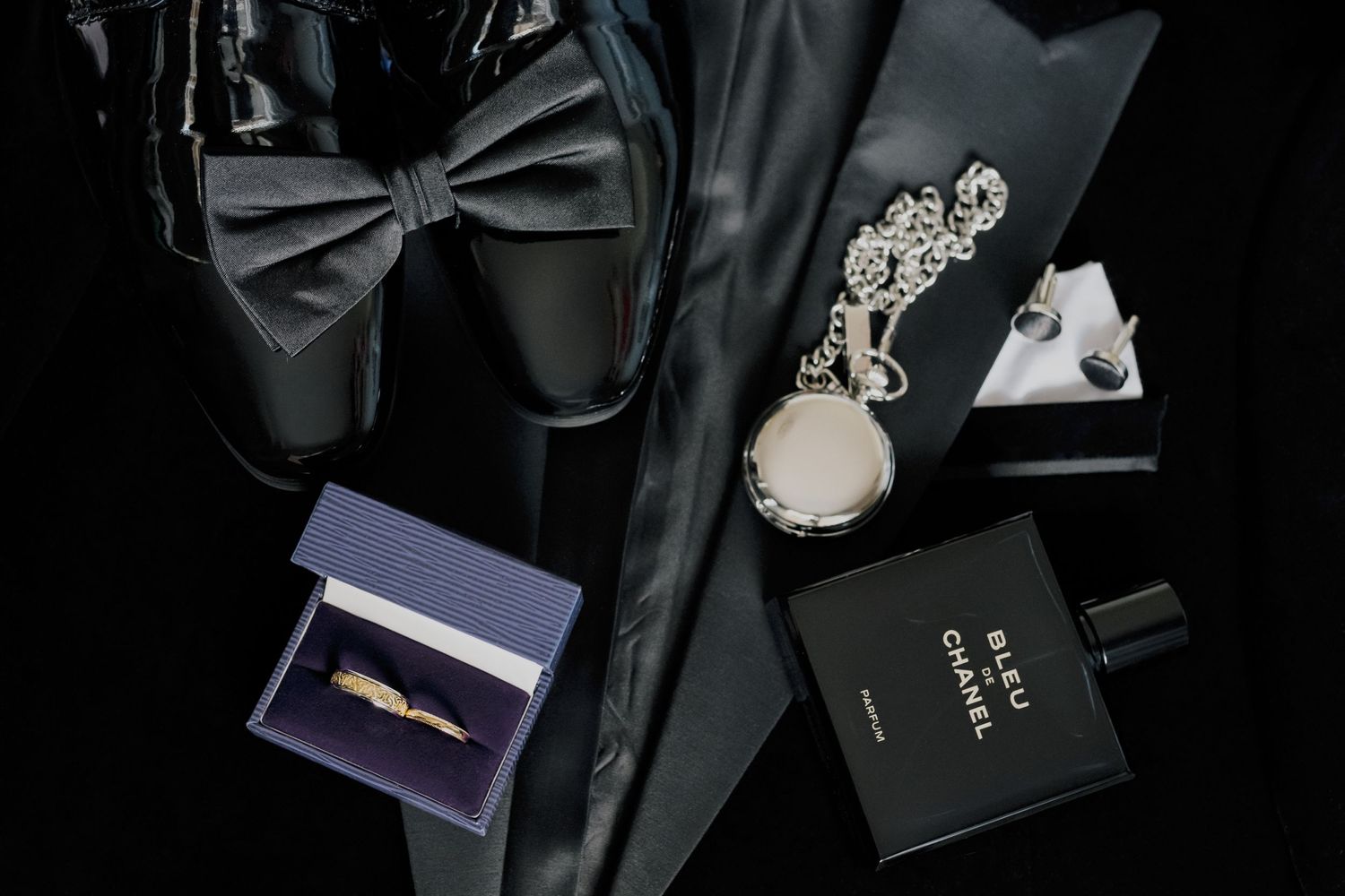Wedding accessories including a black bowtie, jewelry, and perfume arranged on a dark surface, Ireland.