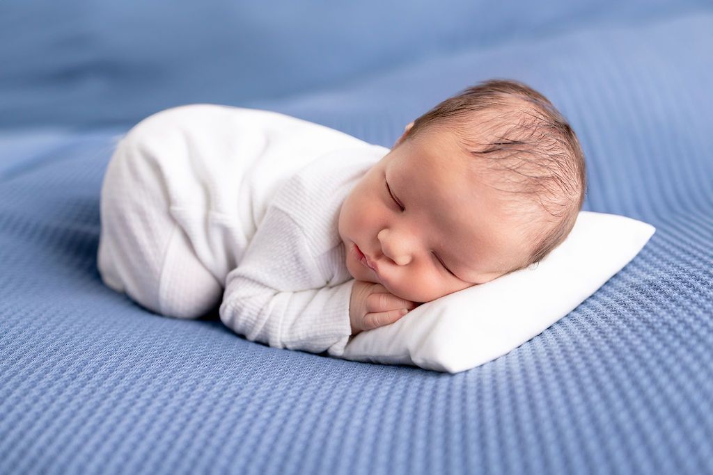 Professional newborn portrait with baby in white wrap against blue textured backdrop.