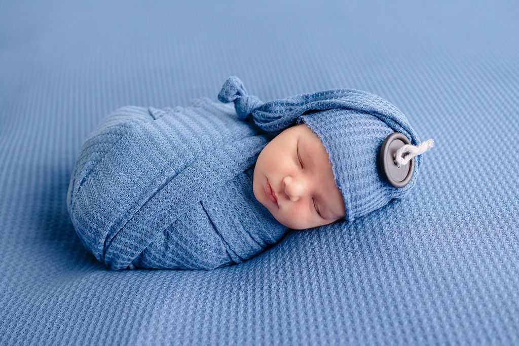 Artistic newborn photo with baby wrapped in blue fabric against matching textured background.