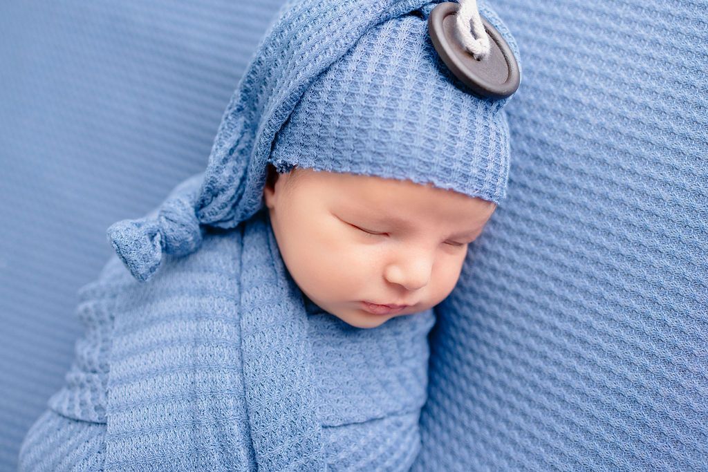 Newborn dressed in blue rests peacefully on a blue textured surface during a photo session.