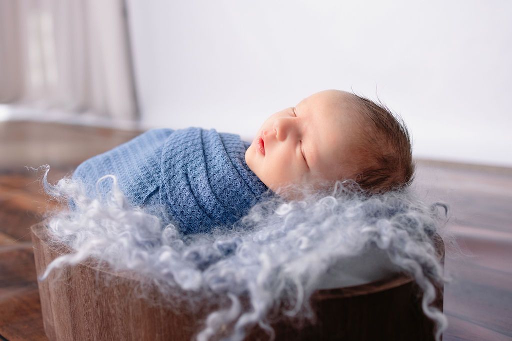 Peaceful sleeping newborn wrapped in blue knit fabric against white background with grey accents.