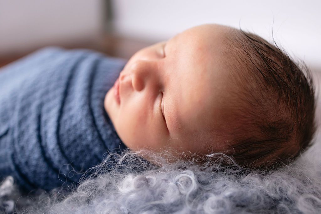 Side profile of sleeping newborn in blue wrap against white backdrop during photography session.