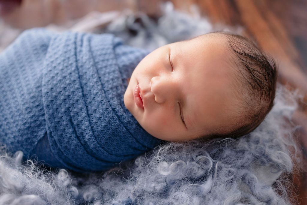 Peaceful newborn portrait with blue wrap and grey decorative fluff on wooden background.