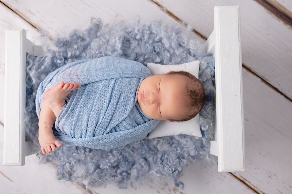 Artistic newborn photography with baby in blue wrap on white wooden planks with grey accents.