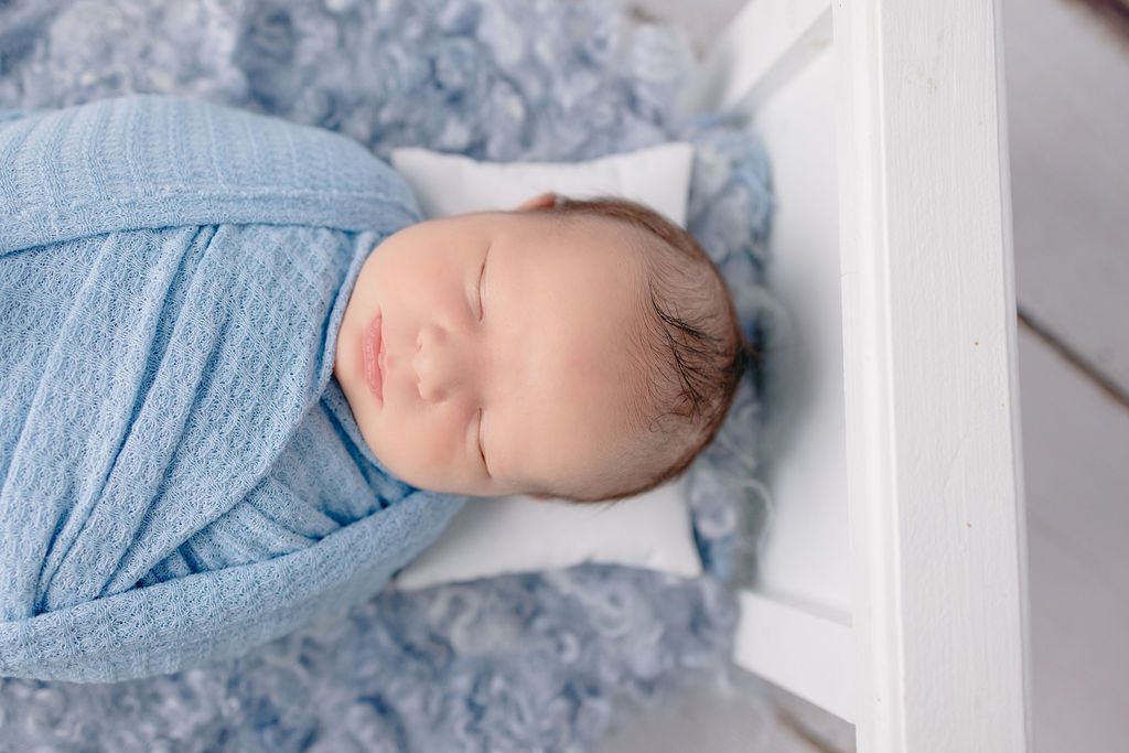 Newborn baby sleeping peacefully on soft blue blanket in peaceful nursery setting.