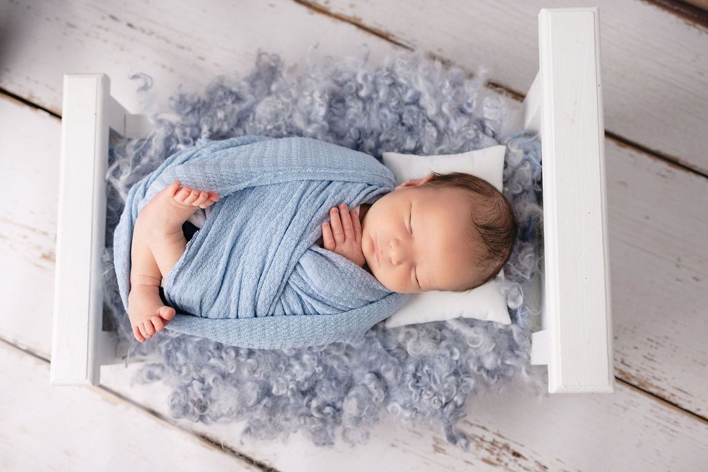 Infant sleeping on white wooden platform with soft blue wrapping.