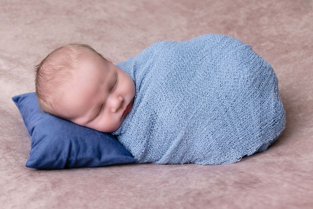 Sleeping baby wrapped in blue blanket on Brown textured surface.