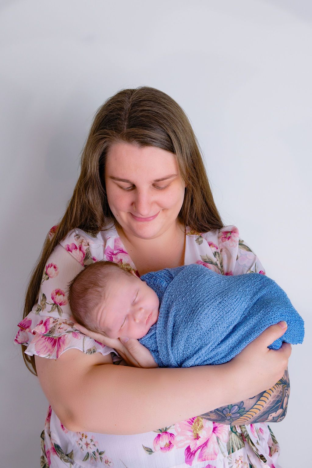 Mother in floral dress holding sleeping baby wrapped in blue blanket.