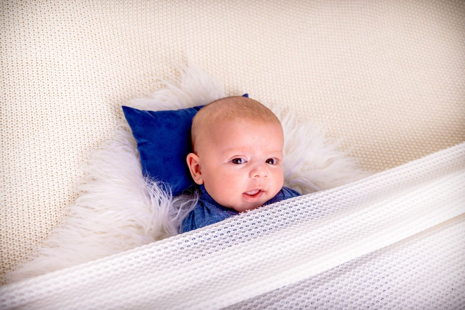 Six sequential images show a baby lying on white bedding with a blue pillow making increasingly expressive looks.
