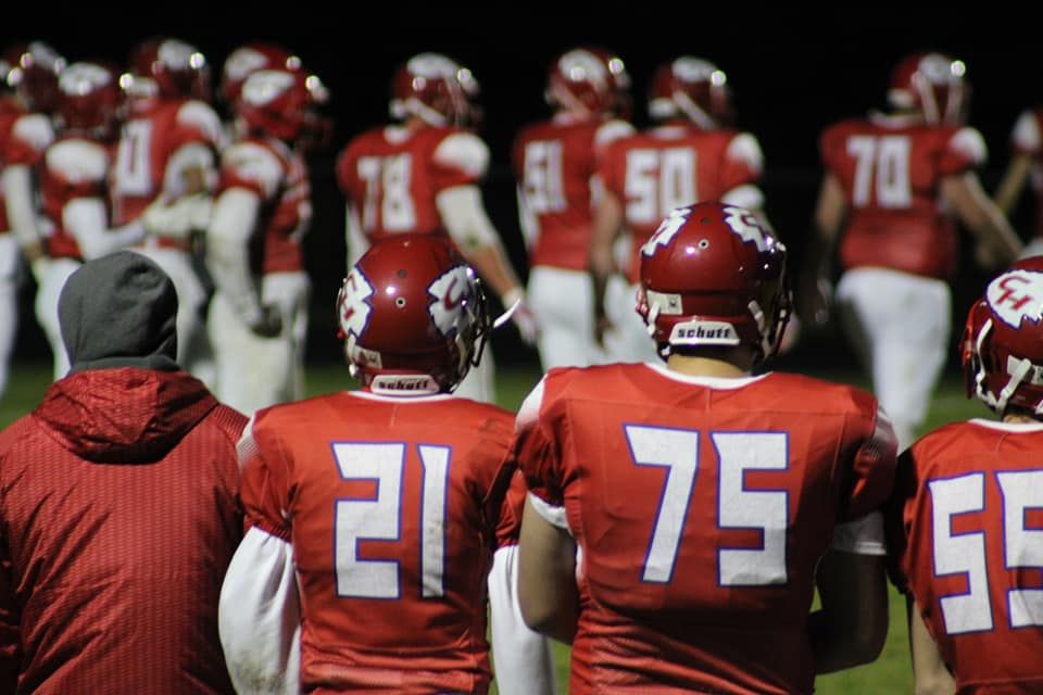 Red-uniformed football players wearing jerseys numbered 21, 75, and 55 stand on the sideline during a night game.
