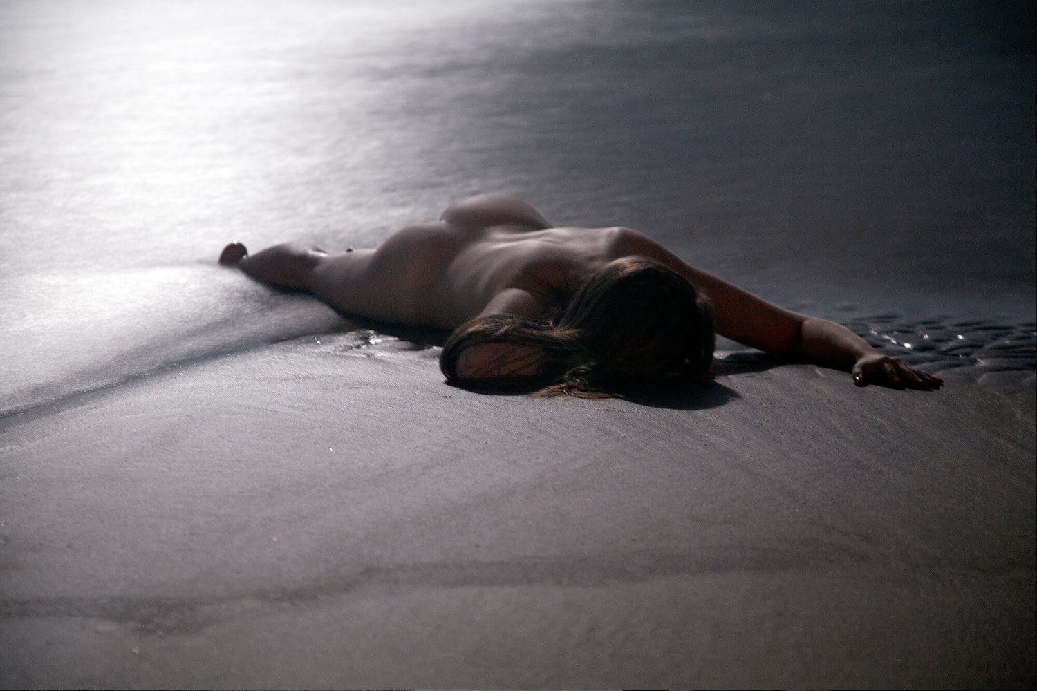Artistic low-key photo of reclining figure on dark reflective surface.
