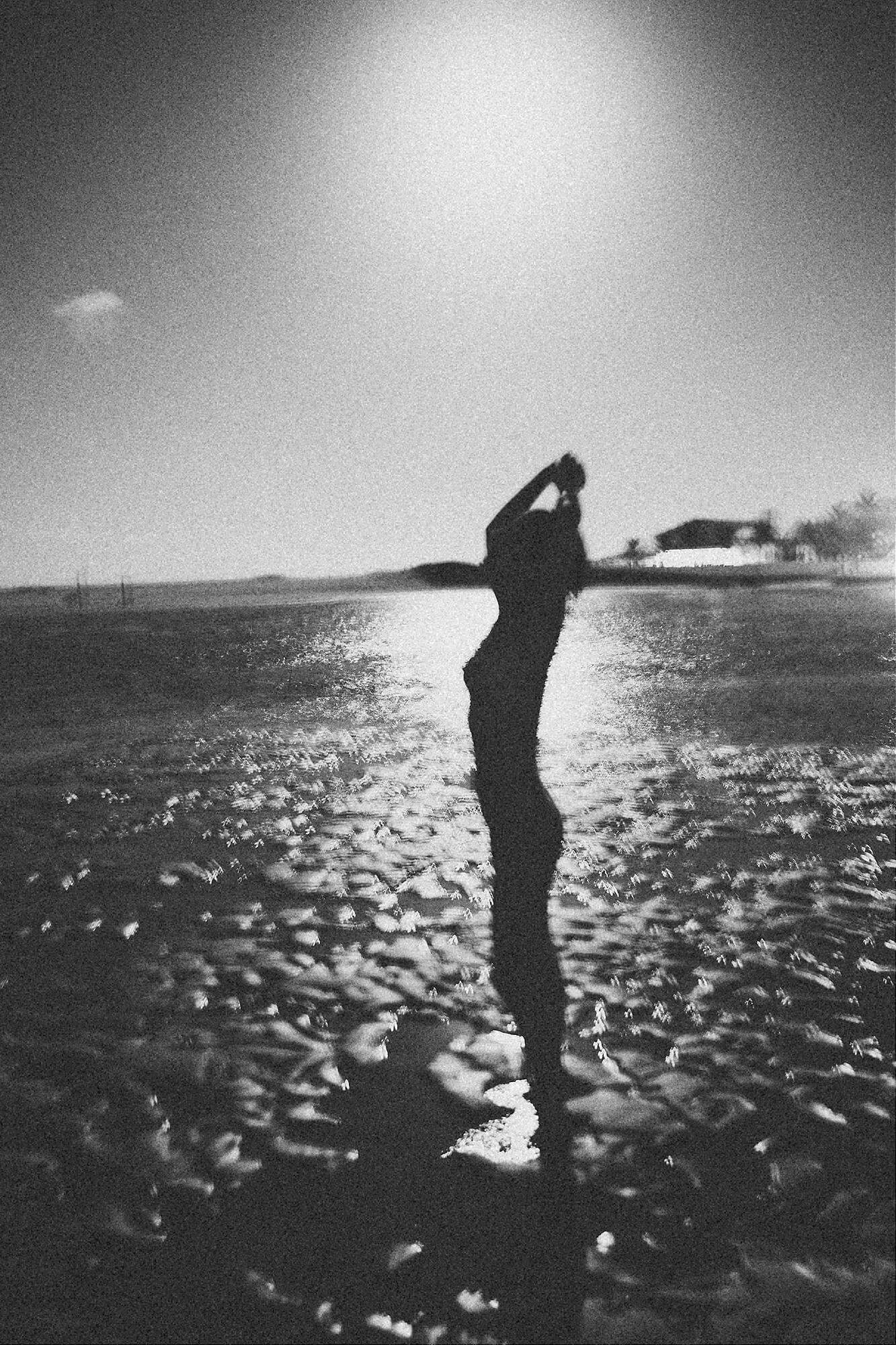 Silhouette of figure stretching against sparkling water at sunset.