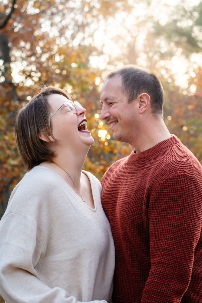 Couple sharing genuine laughter together during autumn photo session outdoors.