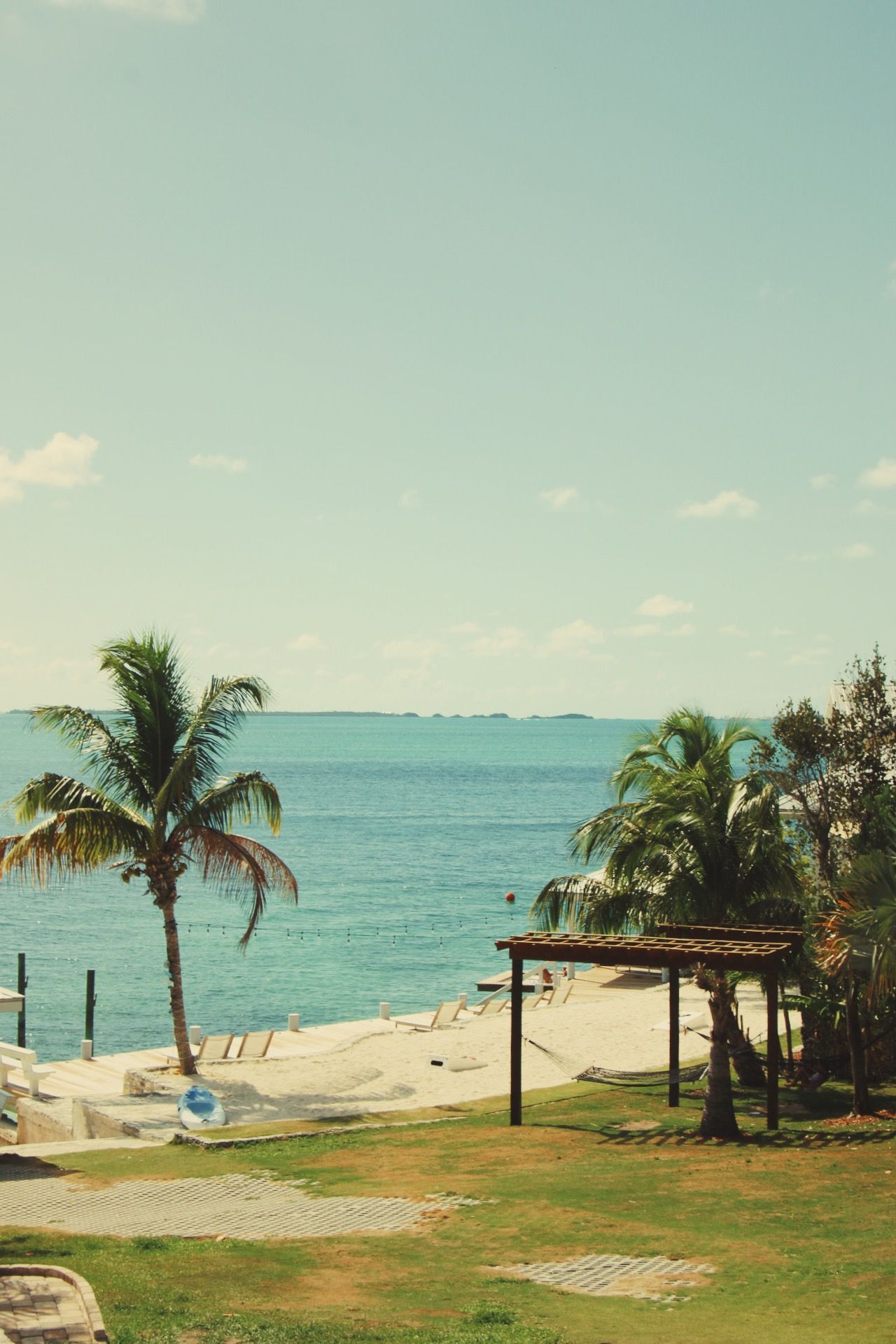 Palm trees frame a beachfront view with turquoise waters and distant islands.