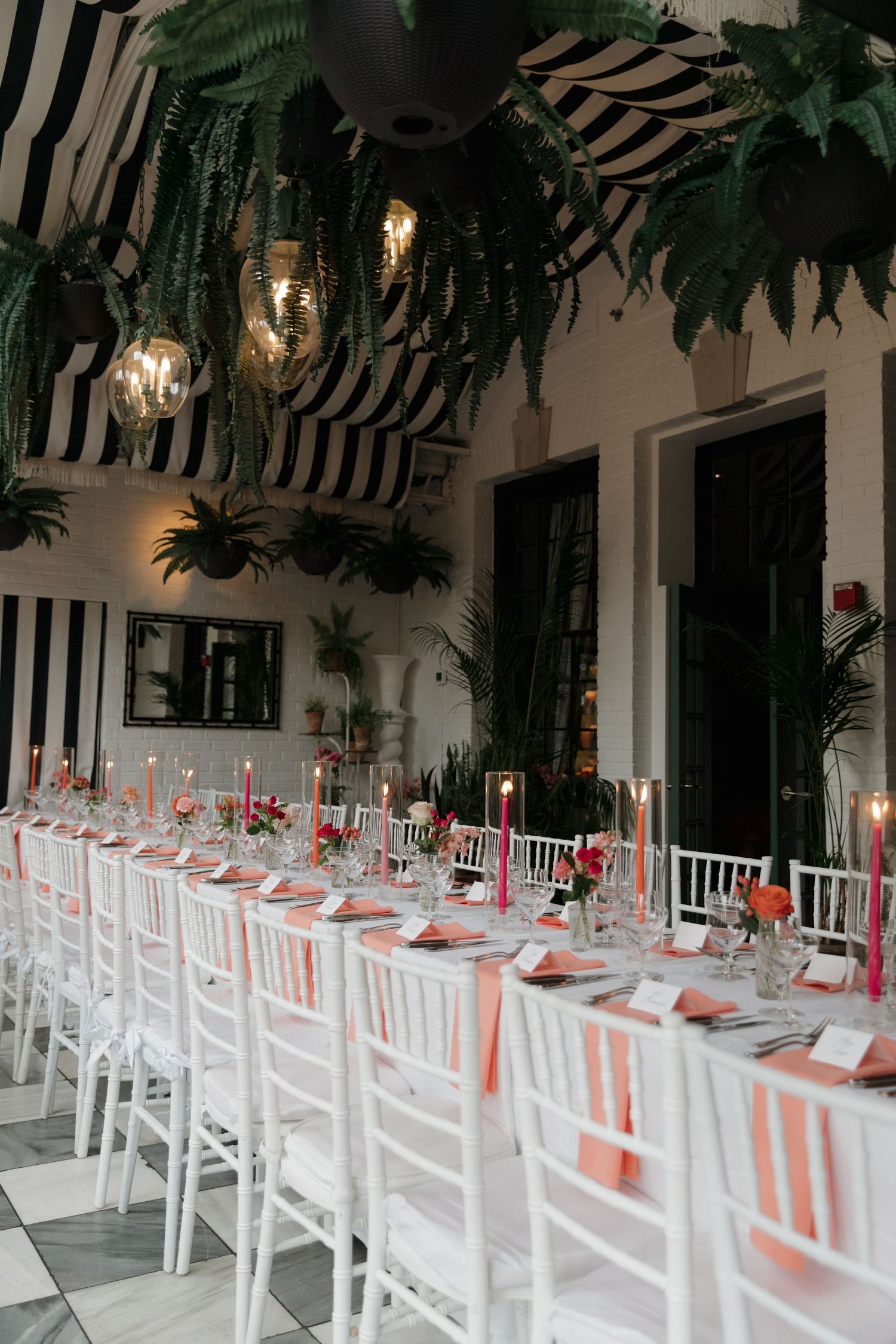 Long white dining table setup with white chairs and coral and pink accents for an elegant wedding reception in a mansion in Rhode Island.