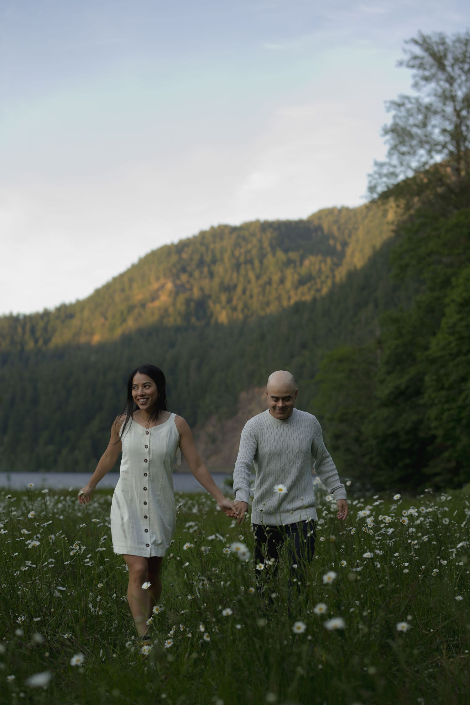 A couple walks through a wildflower meadow with mountains and a lake in the background.