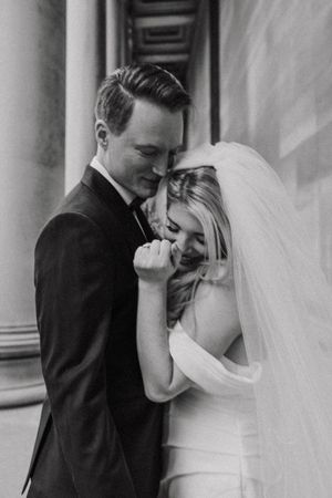 A black and white intimate wedding portrait showing a tender moment between newlyweds in formal attire.