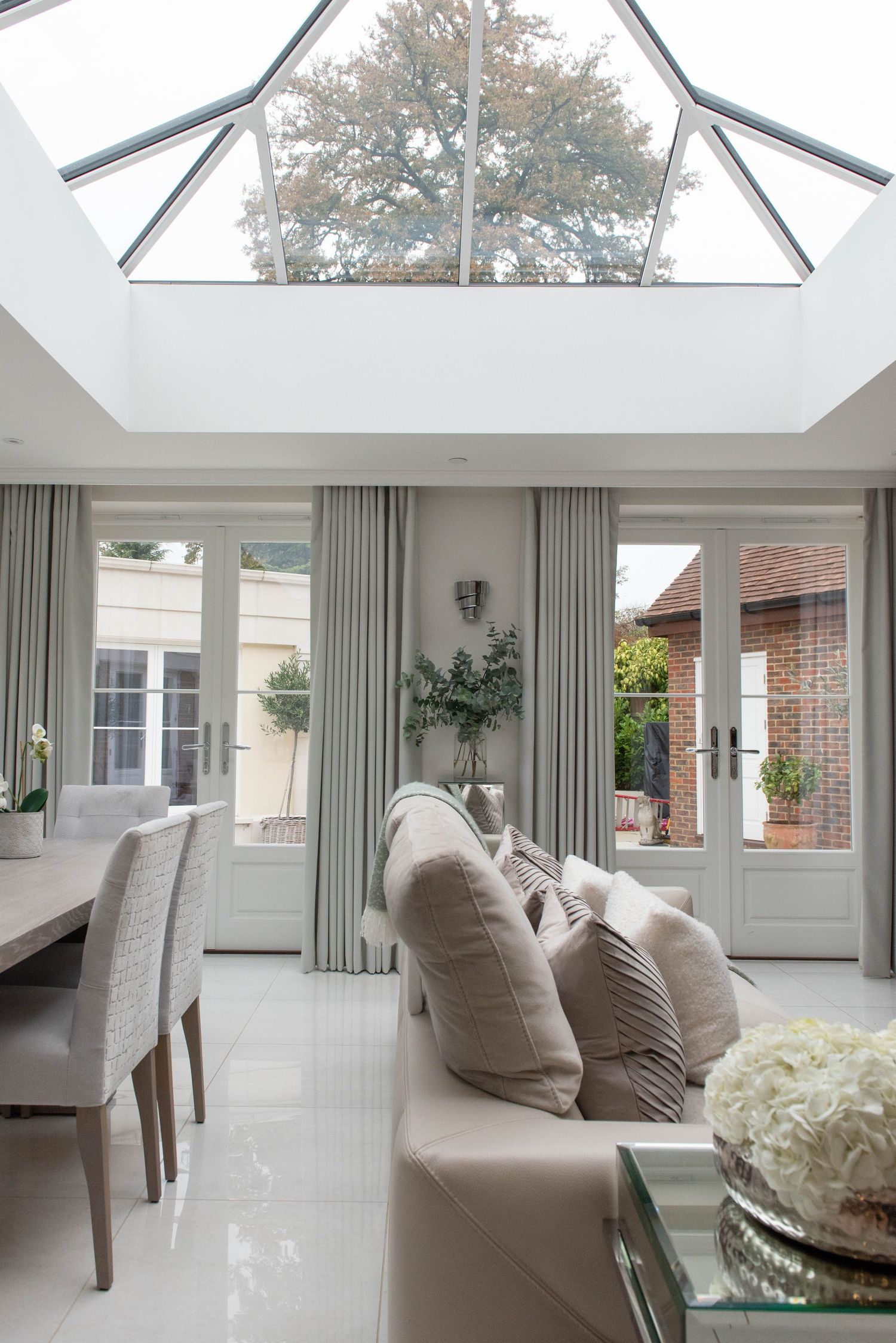 Modern conservatory room with skylights, grey curtains, and comfortable neutral seating showcasing bright natural lighting.