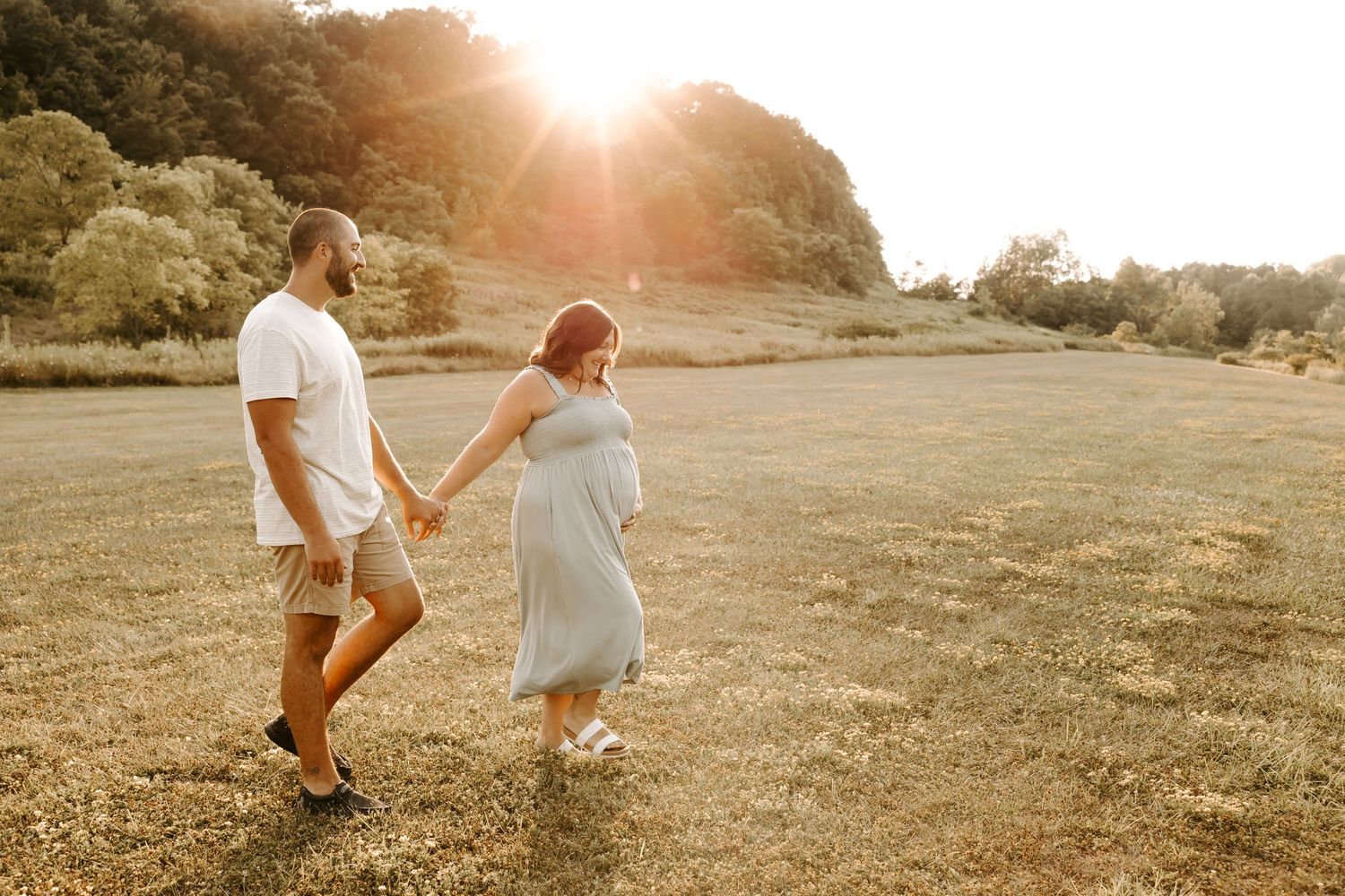 Couple walking hand in hand through sunlit field at golden hour.