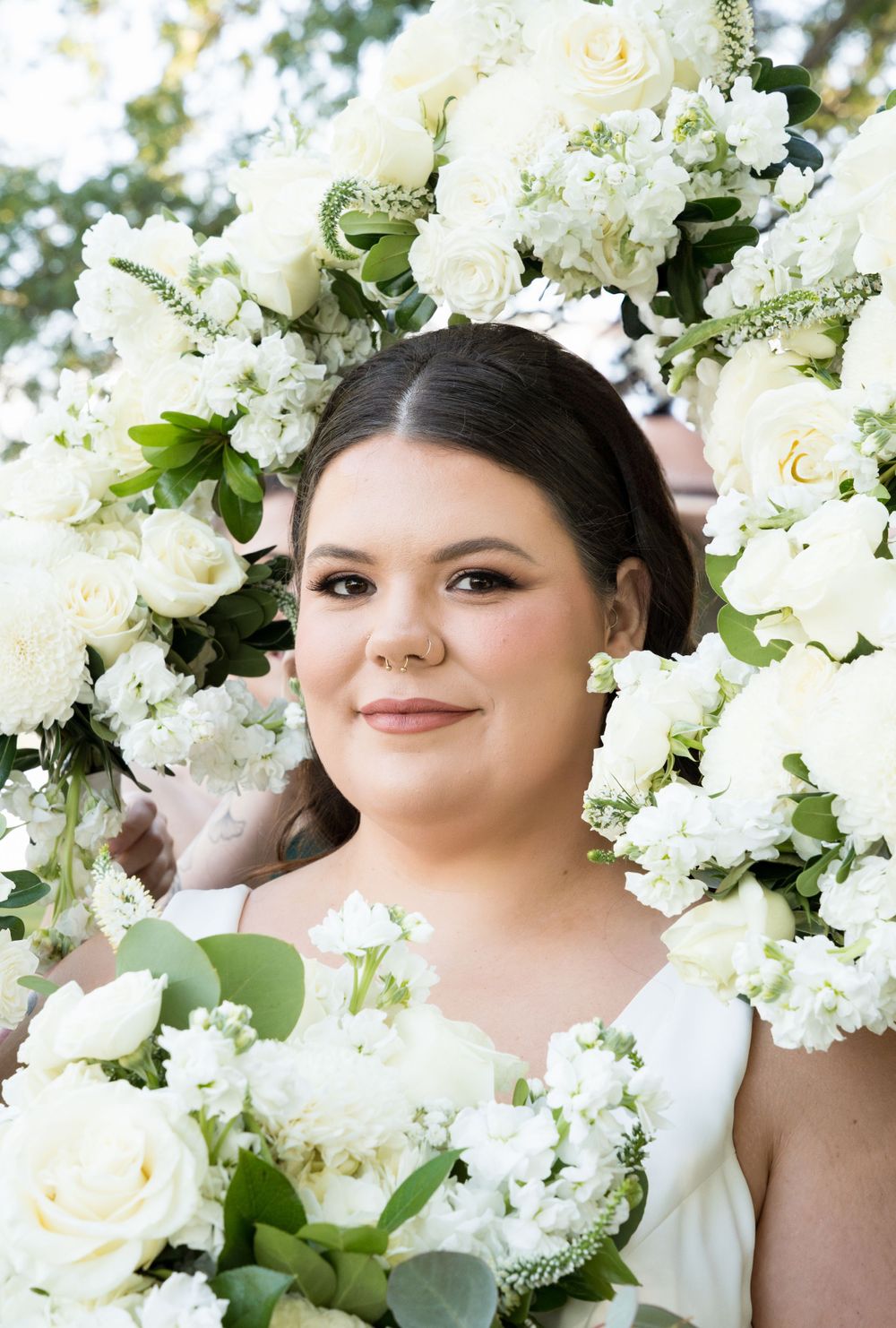 A close-up bridal portrait surrounded by an elegant arrangement of white roses, hydrangeas and greenery.