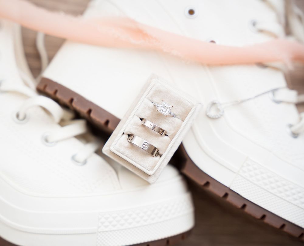 Elegant wedding rings displayed in grey box beside white sneakers and delicate lace details.