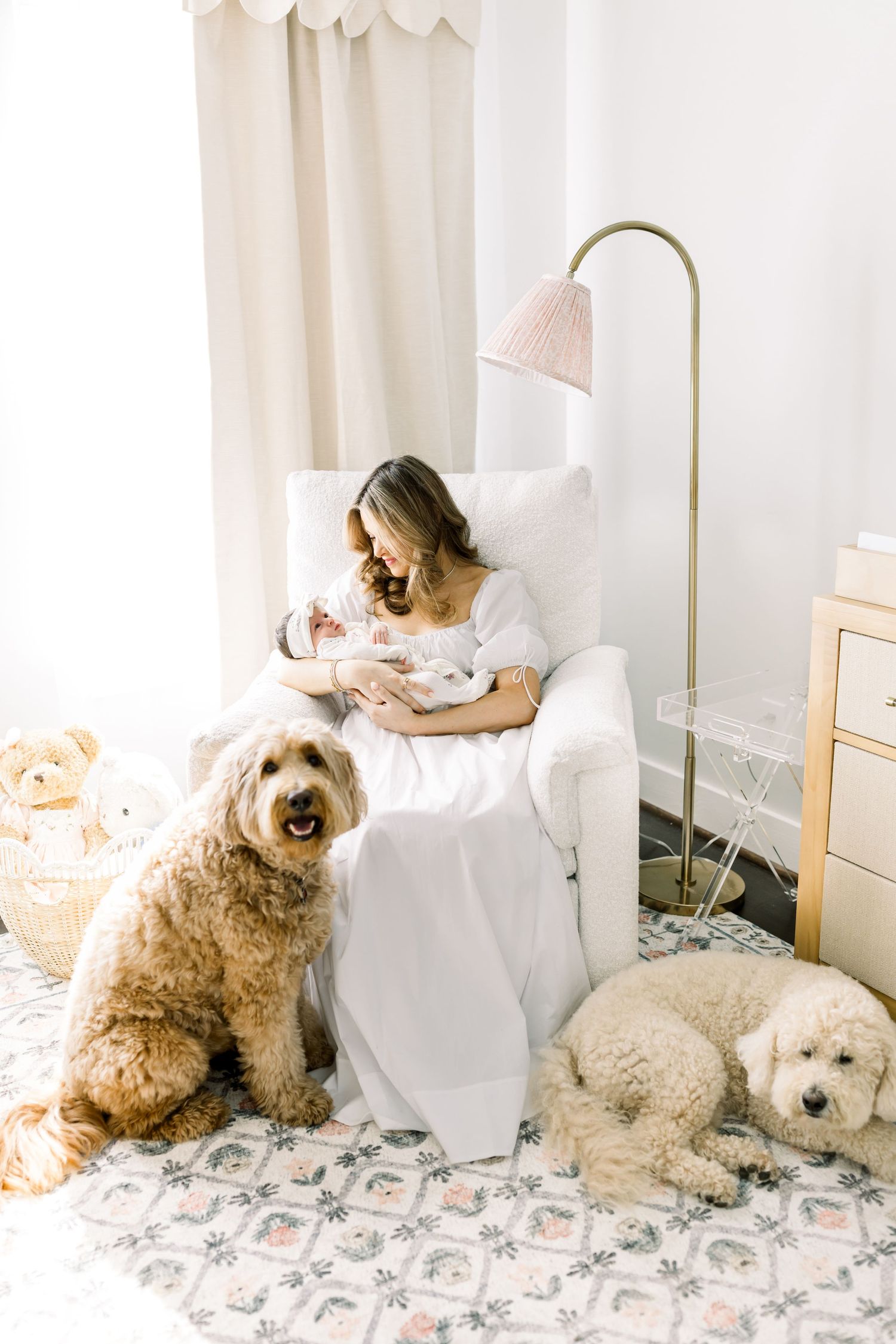 Two fluffy dogs rest beside a white armchair in a cozy nursery with soft lighting.