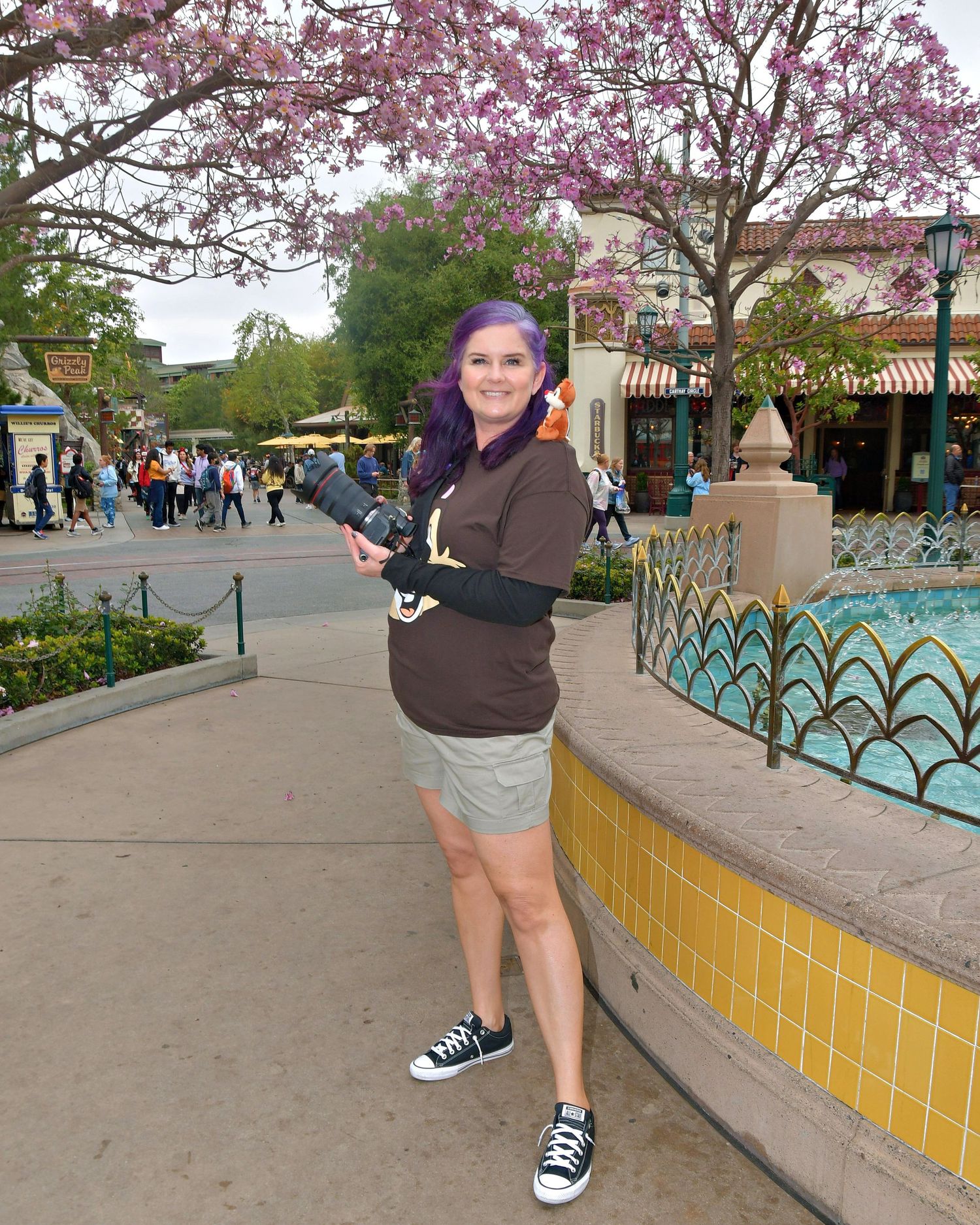 A visitor poses near blooming pink spring trees and decorative tiles at a theme park.