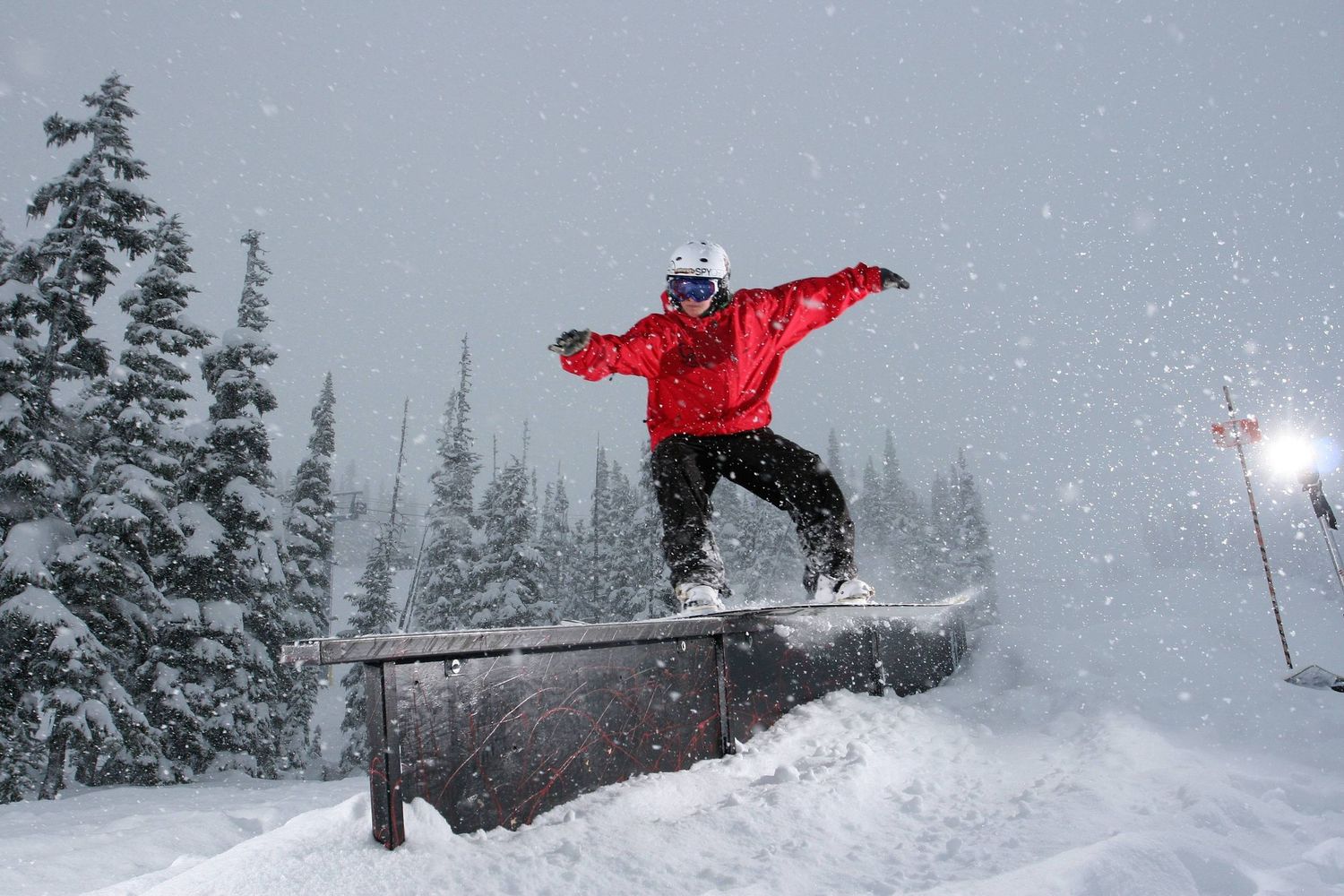 Snowboarder in bright red jacket executes jump over rail in snowy forest conditions.
Whistler Blackcomb