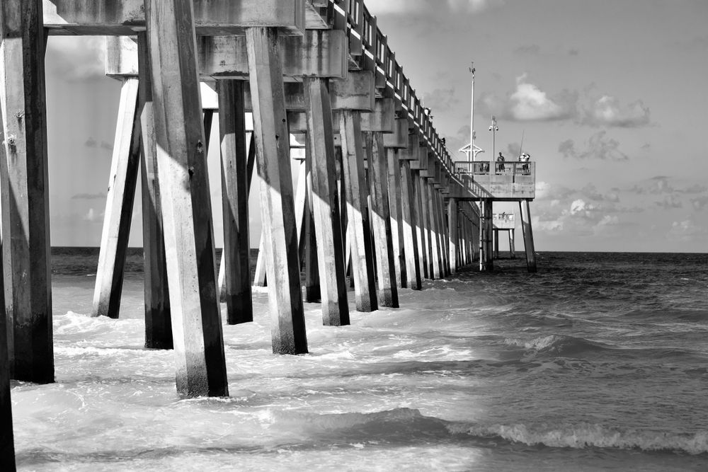 Black and white photograph of wooden pier extending into choppy ocean waters.