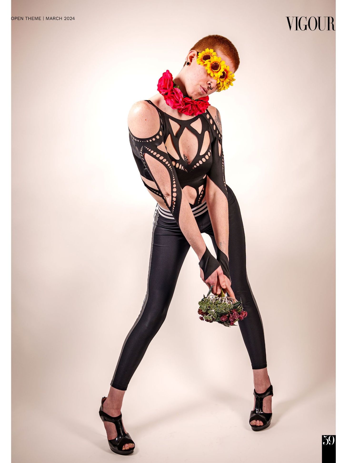 Fashion model poses in black outfit with heels and red flower accessory during studio photoshoot.