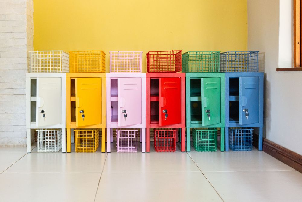 Colorful rainbow lockers with matching baskets stacked against a yellow wall on white tile floor.
