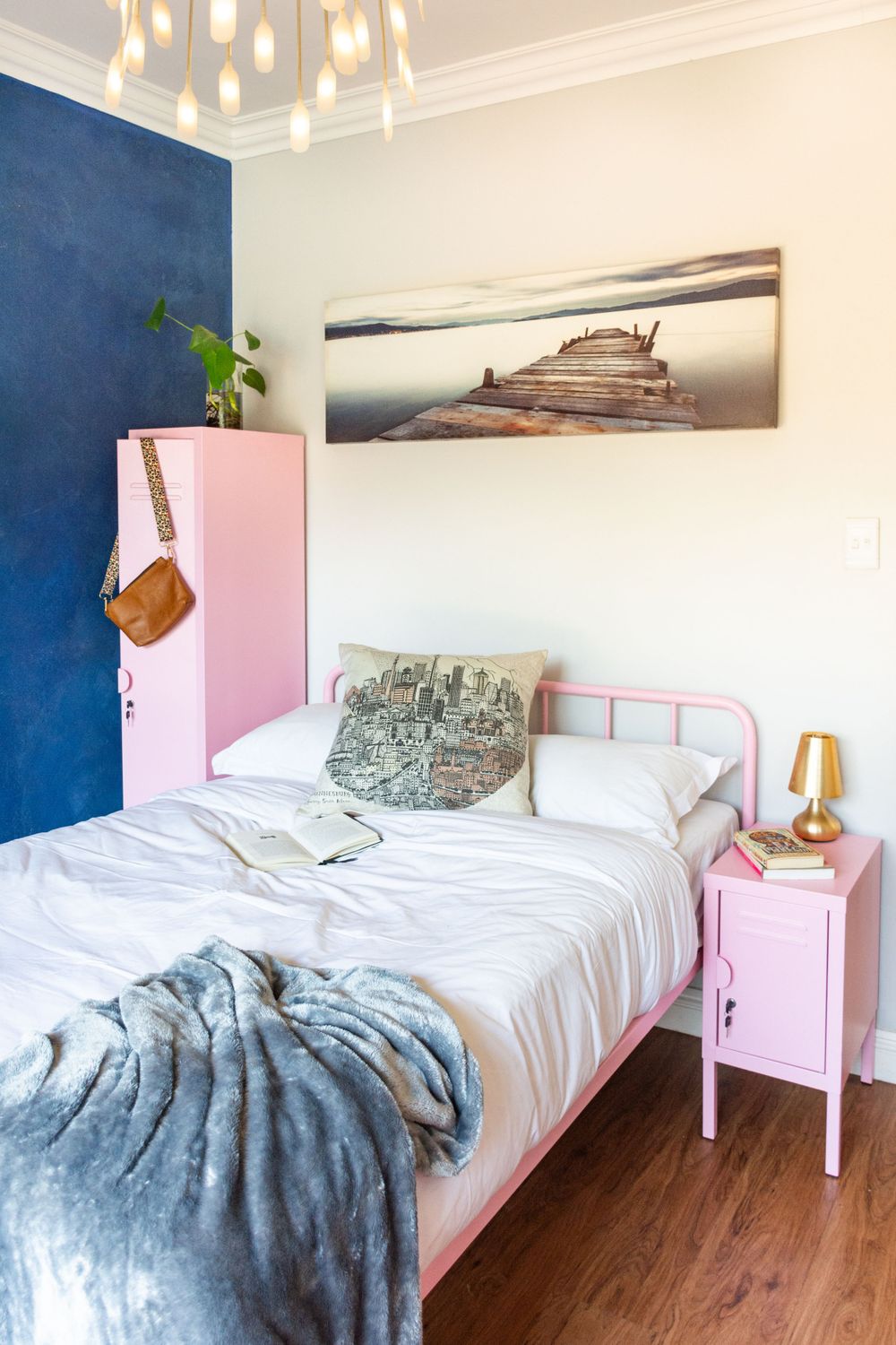 Modern bedroom with pink metal bed frame, blue accent wall, and coastal artwork.