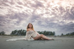 Dreamy maternity portrait on beach with dramatic cloudy sky overhead.