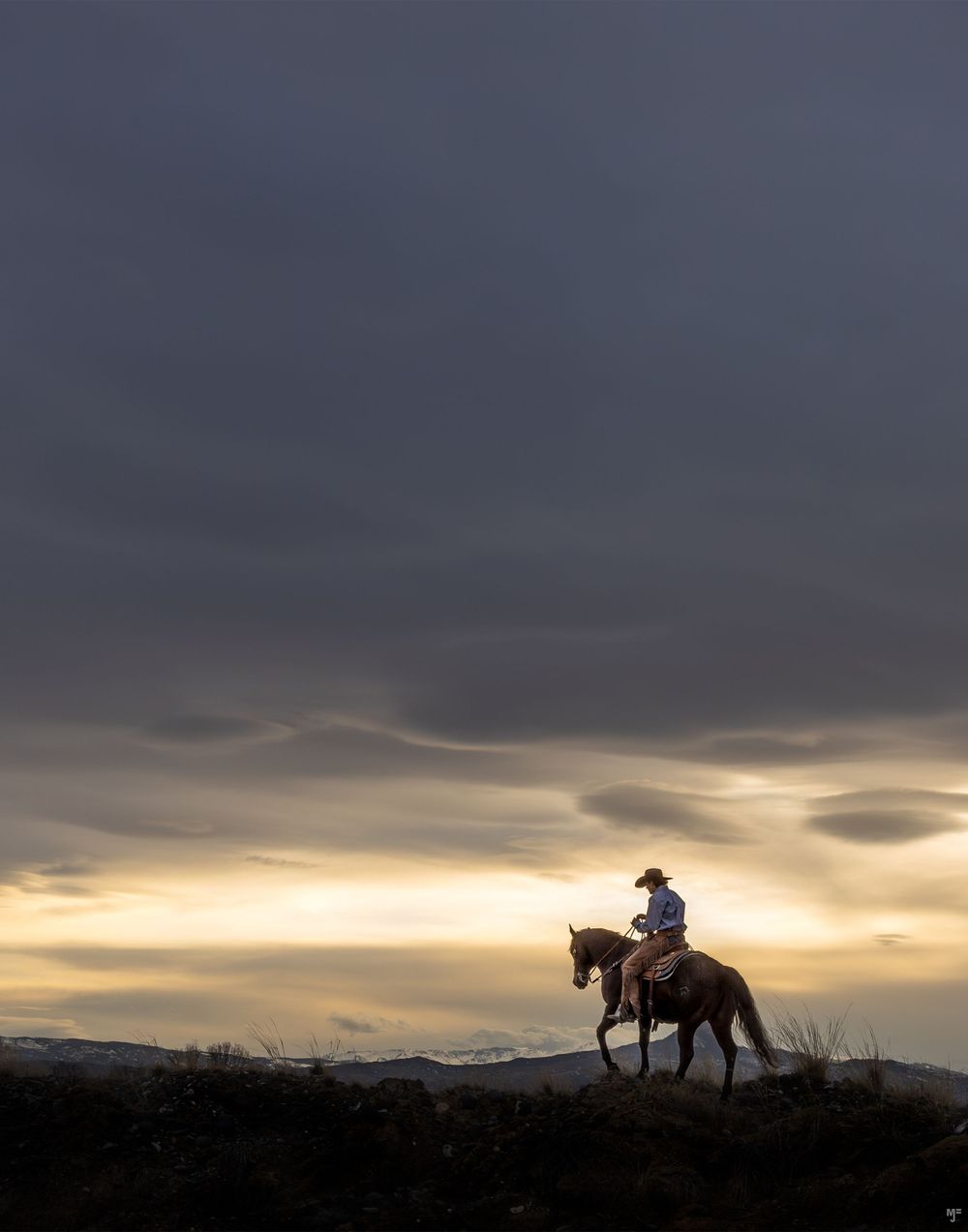 A lone rider on horseback silhouetted against a dramatic sunset sky on a hilltop.