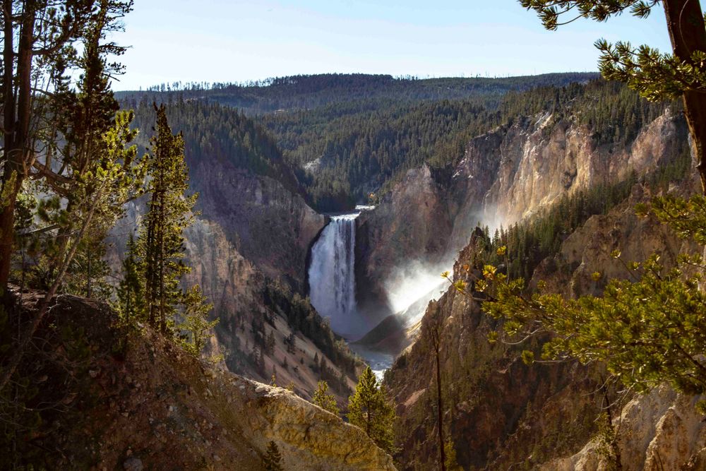 A majestic waterfall cascades through a deep canyon surrounded by forested slopes.