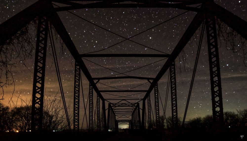 A steel bridge structure silhouetted against a starry twilight sky.