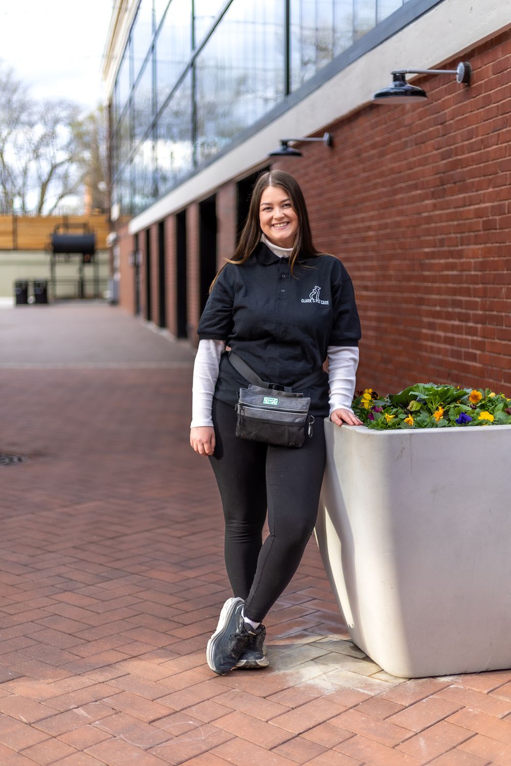 Professional wearing a black uniform stands against a brick wall next to a modern planter with colorful flowers.
